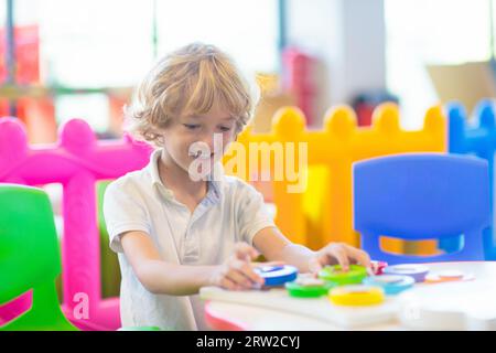 Kleiner Junge im Kindergarten oder in der Kinderbetreuung. Kinder, die im Vorschulalter mit bunten pädagogischen Spielzeugen spielen. Kinder spielen auf dem Hallenspielplatz. Stockfoto