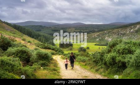Mutter und Tochter laufen auf der Landstraße in Richtung grünes Bergtal. Familienwanderung in Lough Dan, Wicklow Mountains, Irland Stockfoto