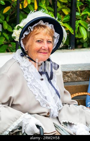 Nahaufnahme einer älteren Dame, die in viktorianischem Kostüm und Motorhaube sitzt. Lächelnd nimmt sie am Broadstairs Dickens Festival Teil. Stockfoto