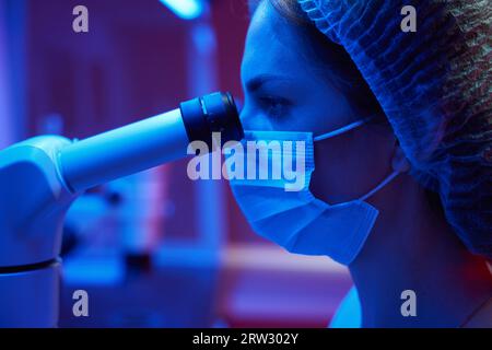 Frau in medizinischer Uniform schaut durch leistungsstarkes Mikroskop-Okular Stockfoto