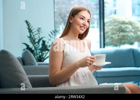 Süße junge Frau, die mit einer Tasse Tee auf einem gemütlichen Sofa sitzt Stockfoto