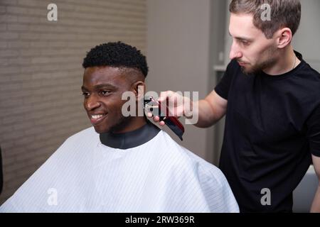 Der fröhliche Afroamerikaner bekommt einen Haarschnitt in einem Friseurladen Stockfoto