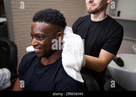 Der freundliche Friseur trocknet die Haare der Gäste mit einem weichen Handtuch Stockfoto