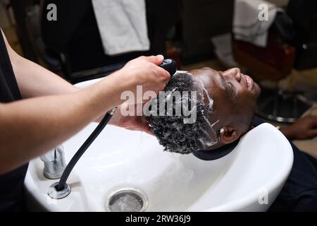 Der Friseur wäscht Schaum von den Haaren des Kunden mit warmem Wasser ab Stockfoto