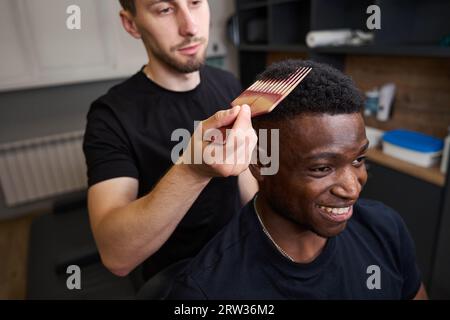 Der Friseur frisiert ein lockiges Haar für afroamerikanische Kunden Stockfoto