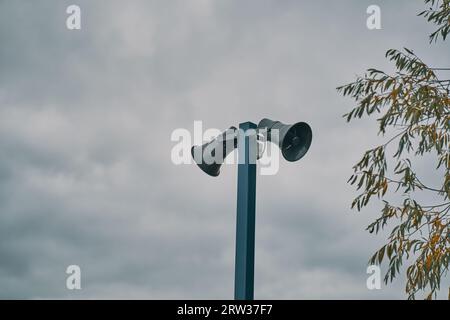 Hohe Metallsäule mit zwei grauen Lautsprechern vor bewölktem Himmel. Warnblinkanlage. Gewährleistung von Sicherheit in der Stadt, Benachrichtigung von Notfällen. C Stockfoto