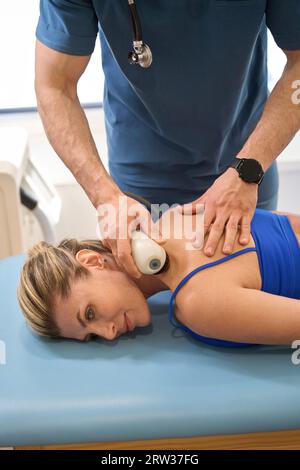 Männlicher Arzt, der extrakorporale Stosswellentherapie bei weiblichen Patienten durchführt Stockfoto