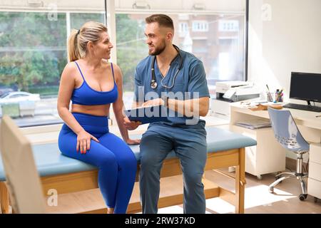 Männlicher Rehabilitologiespezialist spricht mit Frau und zeigt ihren Heilfortschritt Stockfoto