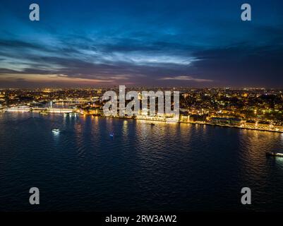 Erstaunliche abendliche Aufnahme von beleuchteten Straßen und Gebäuden in der Stadt. Boote auf der Wasseroberfläche. Nachtleben in der Metropole. Istanbul, Türkei Stockfoto