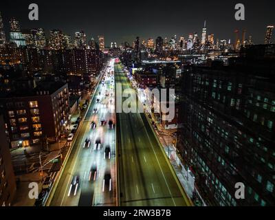 Bewegungsunscharfe Luftaufnahme des Verkehrs auf vielspurigen Schnellstraßen in der nächtlichen Metropole. Wolkenkratzer im Hintergrund. New York City, USA Stockfoto