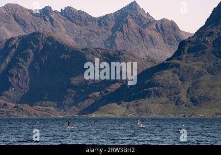 Elgol, Isle of Skye, Schottland. Paddleboarder und Hund mit Cullins im Hintergrund Stockfoto