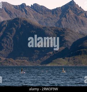 Elgol, Isle of Skye, Schottland. Paddleboarder und Hund mit Cullins im Hintergrund Stockfoto