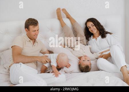Familie mit zwei Kindern auf dem Bett, die Spaß haben. Mather, Vater, Baby und Kleinkinder freuen sich am Morgen im Schlafzimmer. Kinder, die mit ihren Eltern spielen Stockfoto