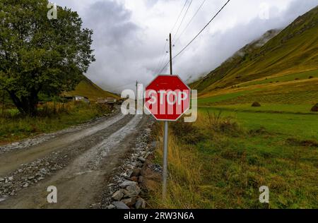 Ein rotes achteckiges Stoppschild auf einer unbefestigten Straße in einer ländlichen Gegend mit klarem blauem Himmel Stockfoto