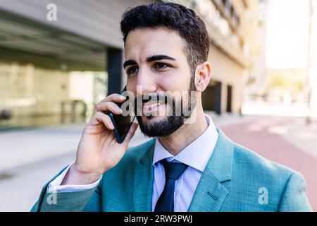 Junger, erwachsener Geschäftsmann, der auf dem Handy spricht, steht im Finanzdistrikt Stockfoto