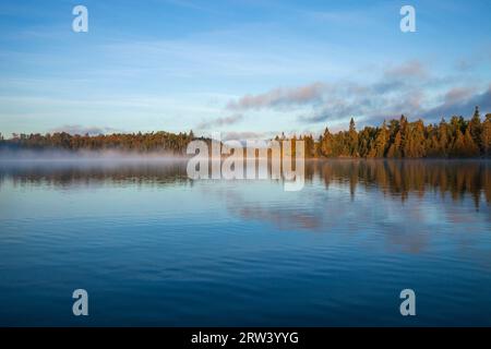 Bäume und Ufer im frühen Morgennebel und Licht auf einem wunderschönen blauen See im Norden von Minnesota im September Stockfoto