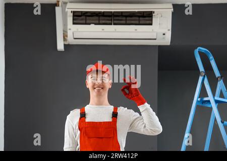 Männlicher Techniker zeigt OK in der Nähe der Klimaanlage im Zimmer Stockfoto