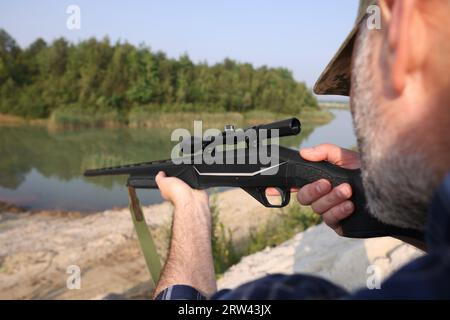 Mann mit Jagdgewehr in der Nähe des Sees, Nahaufnahme Stockfoto