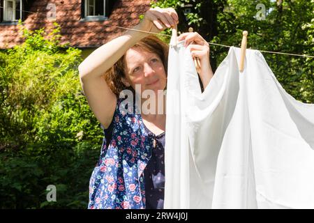 Frau beim Wäscheaufhang im Garten, Frau hängt die Wäsche in einem Garten auf Stockfoto
