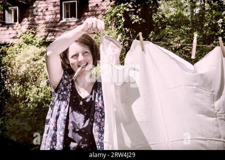 Frau beim Waescheaufhang im Garten, Frau hängt die Wäsche in einem Garten auf Stockfoto