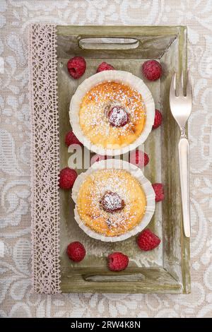 Zwei Käsekuchen-Muffins auf einem Tablett mit Himbeeren und Gabel Stockfoto