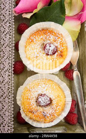 2 Himbeer-Käsekuchen-Muffins auf einem Tablett mit Gabel und Rosenblättern Stockfoto