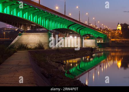 Die Slasko-Dabrowski-Brücke erleuchtete bei Dämmerung mit Reflexionen auf Wasser und Pier auf der Weichsel in Warschau, Polen Stockfoto