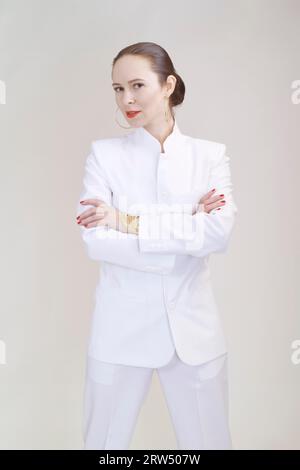 Porträt einer jungen, schönen Frau im weißen Hosenanzug vor grauem Hintergrund Stockfoto