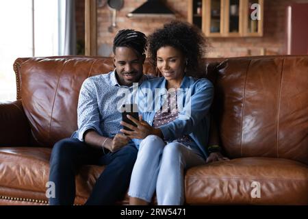 Glückliches afroamerikanisches Paar mit Smartphone, sitzt auf dem Sofa Stockfoto