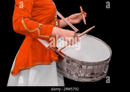 Ein Mädchen in zeremoniellen roten Kleidern spielt mit Schlagstöcken auf einer Trommel auf schwarzem Hintergrund. Stockfoto