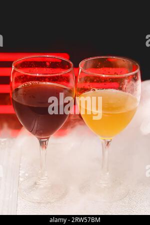 2 zwei Gläser mit alkoholischen Getränken in weißem Shisha-Rauch oder flüssigem Eisrauch auf abstraktem rotem schwarzem Hintergrund. Stockfoto