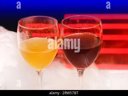 2 zwei Gläser mit alkoholischen Getränken in weißem Shisha-Rauch oder flüssigem Eisrauch auf abstraktem roten blauen Hintergrund. Stockfoto