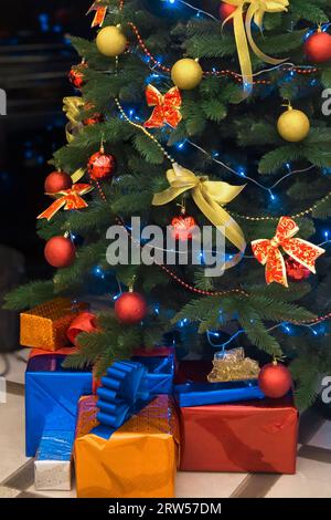 Der grüne Weihnachtsbaum, der mit Spielzeug, Ballons und Bändern mit Geschenken in Kisten verziert ist, ist die Atmosphäre darunter. Stockfoto
