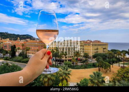 Die Hand der Frau hält ein Glas provenzalischen Roséweins in einem Restaurant im Freien mit einem Hintergrund verschwommener Gebäude in der Altstadt von Nizza, Südfrankreich Stockfoto