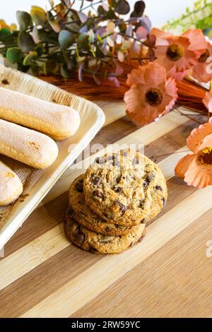 Hausgemachte Plätzchen mit Schokoladenstückchen auf Holztisch mit einigen Blumen und Blättern als Dekoration. Stockfoto