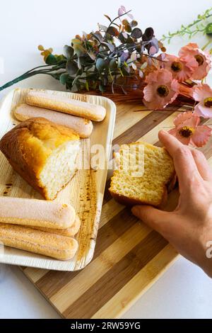 Hausgemachter Biskuitkuchen. Die Hand der Frau hält ein Stück. Dekorierter Tisch. Vertikale Aufnahme. Stockfoto