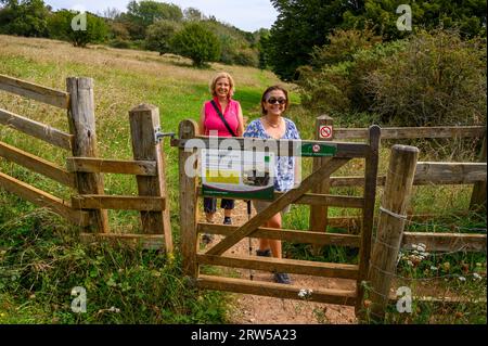 Zwei Frauen mittleren Alters laufen durch ein hölzernes Tor auf dem Weg zum Gipfel des Bow Hill in Kingley Vale, West Sussex, England. Stockfoto