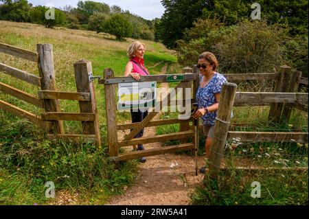 Zwei Frauen mittleren Alters laufen durch ein hölzernes Tor auf dem Weg zum Gipfel des Bow Hill in Kingley Vale, West Sussex, England. Stockfoto