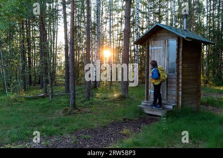 Junge Tourist in der Nähe von öffentlichen Toiletten aus Holz auf dem wunderschönen Wald Mannikjarve Wanderweg in üppigen Kiefernwald im Endla Naturschutzgebiet in Estland Stockfoto