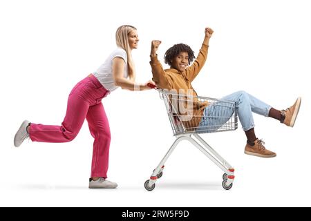 Kaukasische junge Frau, die einen Einkaufswagen mit einem afroamerikanischen Mann in sich schiebt, isoliert auf weißem Hintergrund Stockfoto