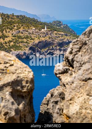 Ein Segelboot gleitet anmutig durch das ruhige Wasser in Port de Sóller, begleitet vom Leuchtturm Far del Cap Gros, der hoch auf den Klippen von steht Stockfoto