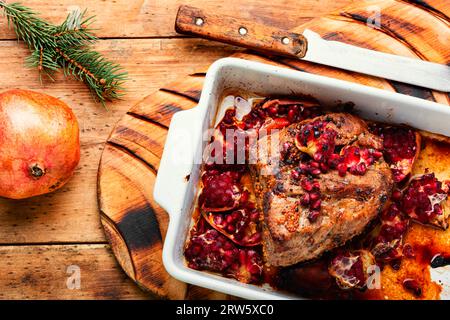 Duftendes Stück Schinken, gebacken mit Granatapfel auf altem Holztisch. Rezepte Fleisch für Weihnachten. Rustikaler Stil. Stockfoto