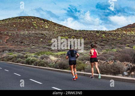 Ein Paar Sportler joggen in den Bergen auf der Straße. Ein Mann und eine Frau trainieren im Sommer gemeinsam, um an einem Marathon teilzunehmen. Junge Leute arbeiten Stockfoto