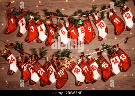 Adventskalender mit Geschenken in den Kindersocken. Zweige eines Weihnachtsbaums, Lichter von Girlanden auf einem hölzernen Hintergrund. 24 Socken des Advents ca. Stockfoto