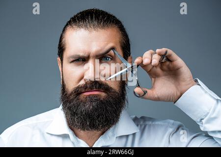 Friseurschere. Vintage Friseurladen, Rasieren. Männchen im Friseurladen, Haarschnitt, Rasieren. Bärtiger Mann isoliert auf grauem Hintergrund. Mans Haarschnitt in Friseur Stockfoto