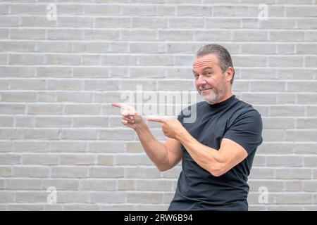 Porträt eines attraktiven freundlichen Mannes, der auf die linke Seite zeigt und auf die Kamera schaut Stockfoto