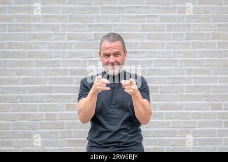 Porträt eines attraktiven freundlichen Mannes, der auf die Kamera vor einer weißen Ziegelwand zeigt Stockfoto