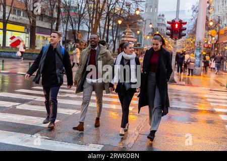 Eine Gruppe von multirassischen, geschäftigen Menschen überquert die Straße, während sie lächeln und reden Stockfoto