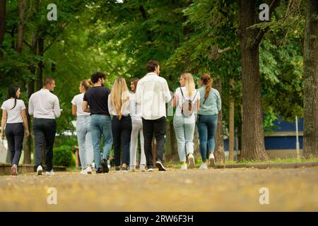 Eine große junge Gruppe von Studenten auf dem Campus, die zusammen mit Büchern und Rucksäcken zur Schule gehen Stockfoto