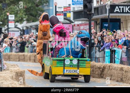 High Street, Colchester, Essex, Großbritannien. September 2023. In der historischen Stadt Colchester findet die erste Seifenkasten-Rallye statt, an der rund 50 Teilnehmer teilnehmen. Die Karts werden über eine Rampe gestartet, um ihnen die Geschwindigkeit zu geben, den Kurs entlang der High Street zu bewältigen, die verschiedene Hindernisse enthält, bevor die Fahrer die Ziellinie erreichen. Das Team namens Going Extinkt trägt Dinosaurier-Kostüme Stockfoto